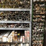 Scaffale metallico pieno di tubi di varie dimensioni e materiali ordinati su pi&ugrave; ripiani, in un magazzino.
