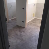 Ampia stanza appena ristrutturata con pavimento in gres porcellanato grigio e pareti bianche e grigie.