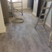Interno di una stanza in ristrutturazione con scale, impalcature e cavi sui pavimenti grigi in vinile.