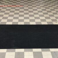 Tappeto nero su pavimento a quadri grigi e bianchi in una stanza con sfondo sfocato. Area ordinata e pulita.