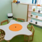 Moquette e Parquet - Tavolo a forma di contenuto uovo di colore bianco e giallo con sedie di legno