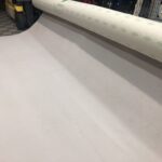 Rotolo di moquette tipologia Nertz carta o tessuto bianco su una macchina in un ambiente industriale o laboratorio di produzione.