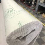 Rotolo di moquette Nerz con marcature su un pavimento a scacchi in un magazzino. Utensili vari dietro.