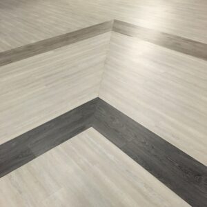 Pavimento in legno con distintive strisce scure parallele che creano un motivo geometrico ad angoli retti.
