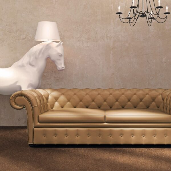 Raffinato salotto con divano chesterfield in pelle marrone chiaro, lampada a forma di cavallo e lampadario classico.