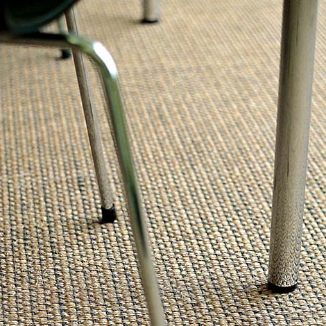 Vista ravvicinata delle gambe di una sedia su un tappeto beige, che mostra il dettaglio della trama del tappeto.