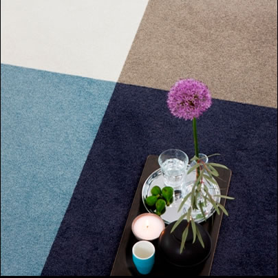 Immagine di una composizione decorativa con una pianta di fiore viola, alcune candele e pietre su una superficie colorata.
