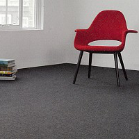 Una sedia rossa moderna con una pila di libri nelle vicinanze, situata in un angolo di una stanza con finestra.