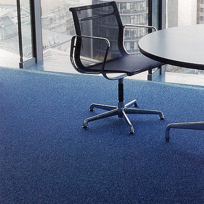 Ufficio moderno con una sedia ergonomica nera vicino a un tavolo rotondo, pavimento blu e vista sulla città.