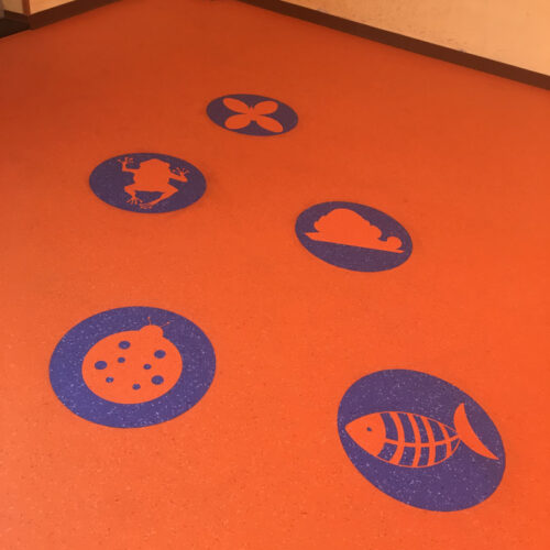 Pavimento arancione con cinque simboli blu raffiguranti un aereo, un'auto, una torta, un pesce e un viso sorridente.