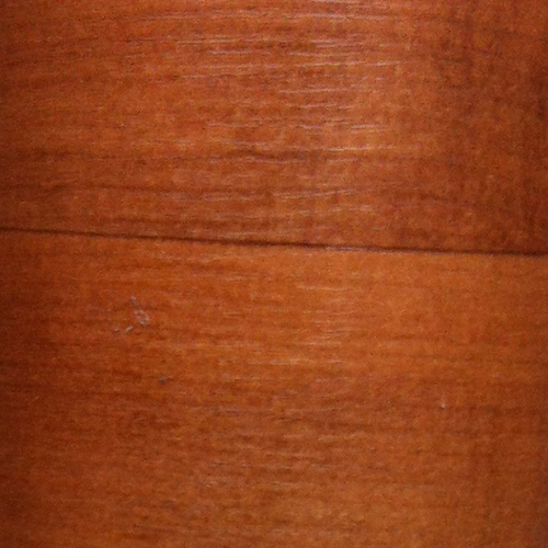 Primo piano di una superficie in legno marrone con evidenti venature e una leggera lucentezza naturale.