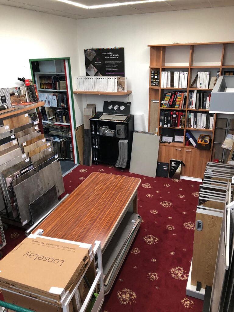 Una stanza con campioni di materiali edili su scaffali e tavoli. Ci sono scatole, libri e riviste esposti. Un ambiente ordinato e accogliente.