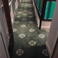 Corridoio di un edificio con moquette verde decorata con motivi bianchi. Pareti bianche con pannelli verdi.