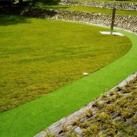 Giardino moderno con prati verdi curati, sentiero di erba sintetica e muretto di pietre lungo il perimetro.