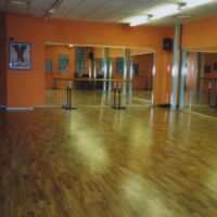 Una sala da ballo con pavimento in legno lucido, pareti arancioni e grandi specchi che riflettono lo spazio.