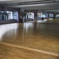 Una sala da ballo vuota con pavimento in legno lucido e grandi specchi alle pareti, pronta per lezioni.