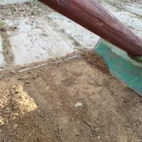 Primo piano di una scopa di saggina su una superficie sporca e polverosa, forse all'aperto con terreno e macerie.