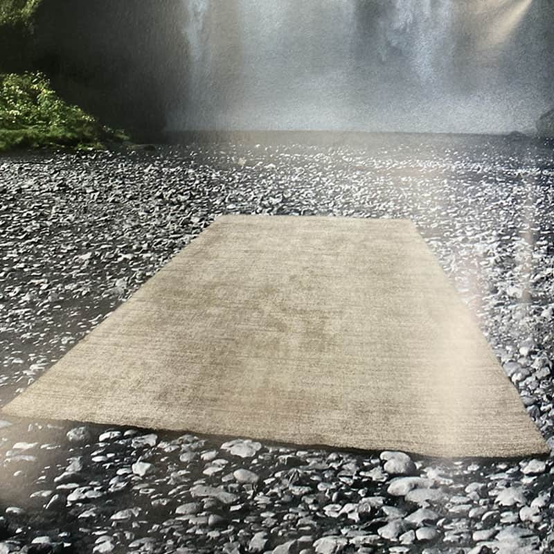 Tappeto tipologia Gabi, realizzato in tencel e lana targato Tisca steso sulla ghiaia in riva ad una cascata 